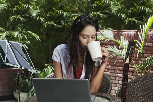 Γυναίκα πίνοντας καφέ και χρησιμοποιώντας ένα φορητό υπολογιστή — Φωτογραφία Αρχείου