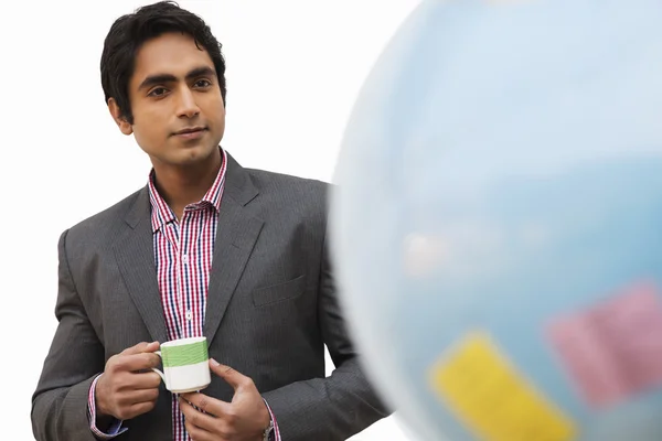 Businessman holding a tea cup and looking at a globe — Stock Photo, Image