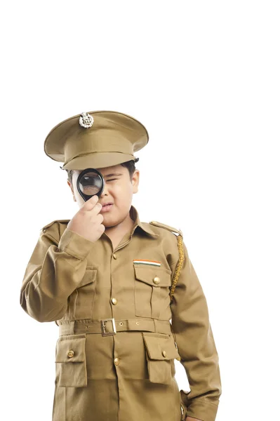 Close-up de um menino vestido como um uniforme da polícia olhando através de uma lupa — Fotografia de Stock