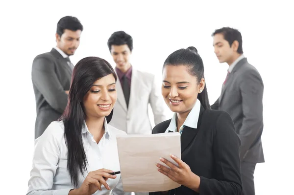 Two businesswomen reading a document with their colleagues in the background — Stock Photo, Image