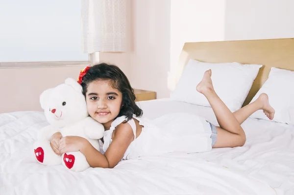 Retrato de una chica acostada en la cama sosteniendo un osito de peluche y sonriendo — Foto de Stock