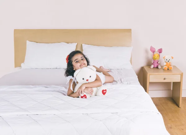 Chica acostada en la cama sosteniendo un oso de peluche y sonriendo — Foto de Stock