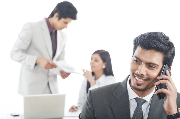 Close-up of a businessman talking on a mobile phone with his colleagues in the background — Stock Photo, Image