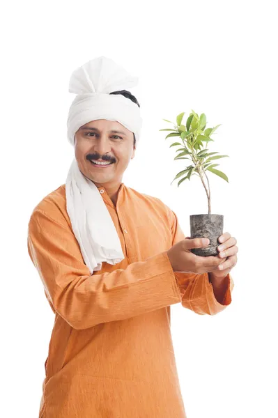 Retrato de un agricultor sosteniendo una planta en maceta y sonriendo — Foto de Stock