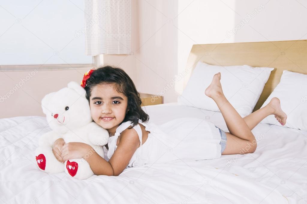 Portrait of a girl lying on the bed holding a teddy bear and smiling