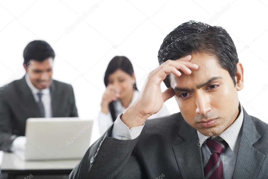 Close-up of a businessman looking upset with his colleagues in the background
