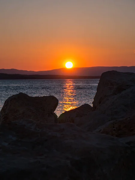 Günbatımında ön planda kayalar ve Hırvatistan kıyılarında dağlar var. Akdeniz 'de bir yaz sahnesi.