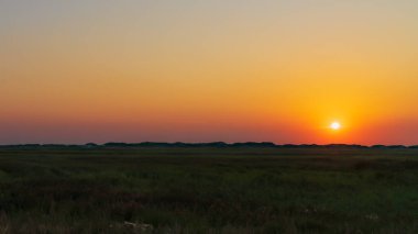 Hendek ve sahil arasındaki çayırların üzerindeki panoramik manzara Kuzey Denizi kıyısındaki derin batan güneşe karşı. Bir Ağustos sahnesi.