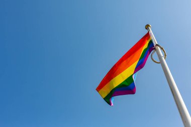 Gökkuşağı LGBT bayrağını parlak ve açık mavi bir gökyüzüne doğru dalgalandırın. Suffolk Gururu. Mutluluk kavramı. Özgürlük. Eşcinsel çift.