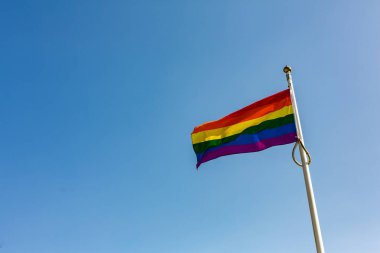 Gökkuşağı LGBT bayrağını parlak ve açık mavi bir gökyüzüne doğru dalgalandırın. Suffolk Gururu. Mutluluk kavramı. Özgürlük. Eşcinsel çift.