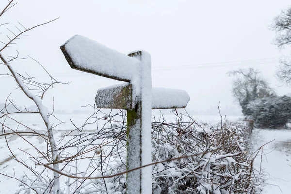 A countryside sign post that displays public footpaths totally covered in snow and unreadable