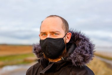 Covid-19 Corona salgını sırasında siyah yıkanabilir yüz maskesi takan genç bir adam.