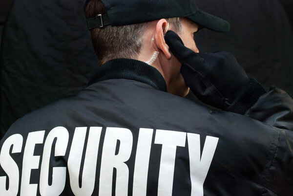 Security Guard Listens To Earpiece, Back of Jacket Showing