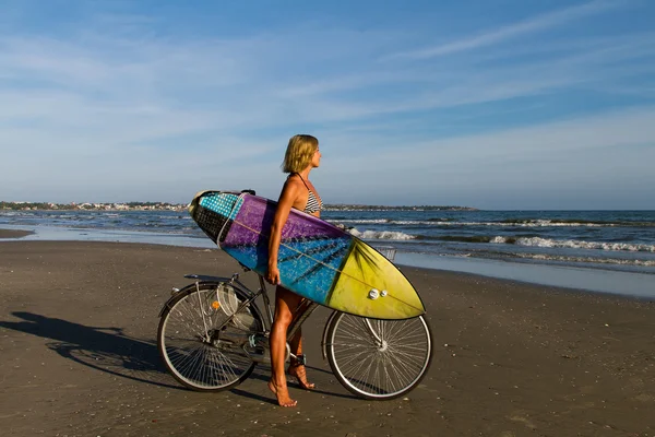 Femme sur un vélo avec un surf — Photo