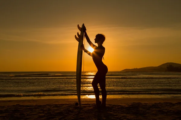 Rear view of beautiful sexy young woman surfer girl in bikini with white surfboard on a beach at sunset or sunrise — Stock Photo, Image