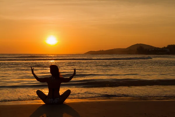 在日落时练瑜伽海洋沙滩上的女人. — 图库照片#