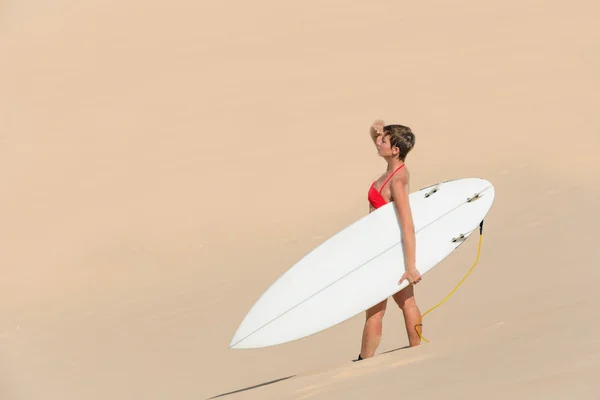 Güzel seksi genç kadın sörfçü kız bikini beyaz surfboard ile çölde bir plajda dikiz — Stok fotoğraf