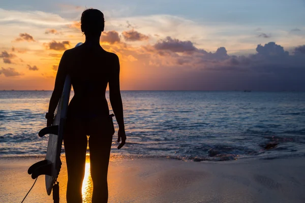 Kobieta internauta z deską surfingową na tropikalnej plaży o zachodzie słońca — Zdjęcie stockowe