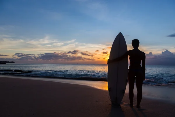女人的冲浪者，以在日落时分的热带海滩上的冲浪板 — 图库照片