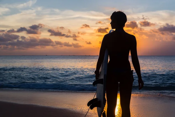 Woman surfer with surfboard on tropical beach at sunset — Stock Photo, Image