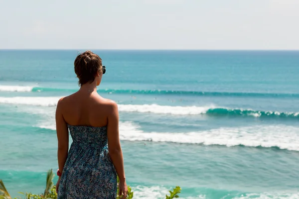 Bella donna in piedi sul bordo della roccia e in cerca di surfisti — Foto Stock