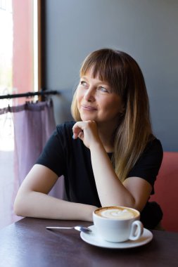 Gülümseyen kadın bir fincan kahveyle kafede dinleniyor..