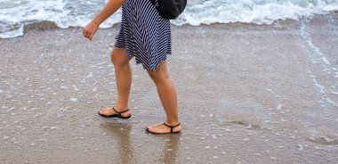 Bir kız deniz boyunca ıslak kumda yürür.