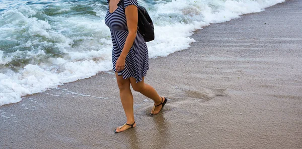 Bir kız deniz boyunca ıslak kumda yürür.