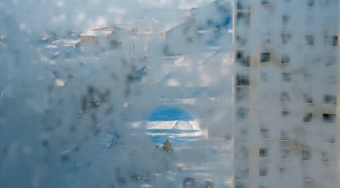 Binanın içinden soğuk hava koşullarında çekilmiş, çok katlı bir binanın, donmuş bir camın içinden görüntüsü.