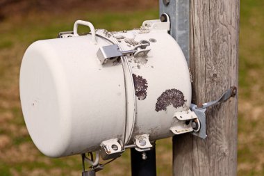 Tahta bir direğe bağlı beyaz metal varil.