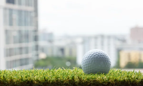 Bola de golfe na grama verde com fundo de construção — Fotografia de Stock