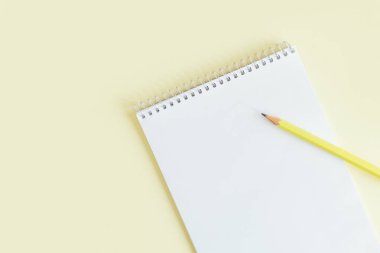 Sarı pastel arka planda boş sayfa ve kalem olan defter. Düz yatıyordu. Metin için yer. 