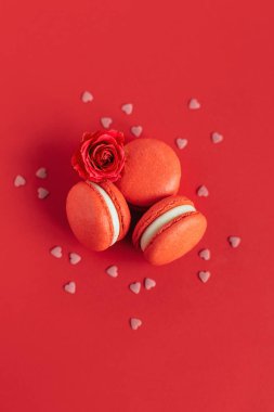 Kırmızı arka planda gül çiçekli kırmızı Fransız kurabiyeleri. Sevgililer Günü için konsept. Mesaj için yer. Düz yatıyordu.