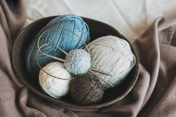 Шкафы и шарики из шерстяной пряжи и вязаные иглы для ручного вязания в корзине. Естественные цвета. Концепция ручной работы.