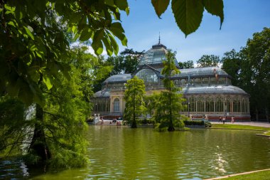 Madrid, İspanya, 20 Haziran 2018: El Retiro Park 'taki Cam Saray Louisiana' dan gelen selvi ağaçlarıyla dolu küçük bir göletin yanında duruyor. Dökme demirden yapılmıştır.. 