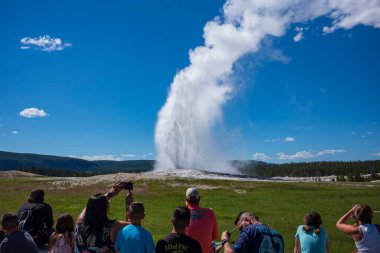 Mamut, WY, ABD - 27 Haziran 2022: Ziyaretçiler, güneşli bir günde, ABD 'nin ilk ulusal parkı olan Yellowstone Ulusal Parkı' nda ünlü gayzer Old Faithful 'u izliyorlar..