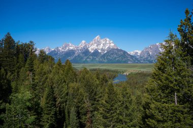 Grand Teton Ulusal Parkı 'nın sıradağları, arka planda açık gökyüzü ve ön planda ahşap çitlerle bir sabah boyunca fotoğraflanır..  