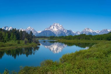 Grand Teton Ulusal Parkı 'nın sıradağları, arka planda açık gökyüzü ve ön planda ahşap çitlerle bir sabah boyunca fotoğraflanır..  
