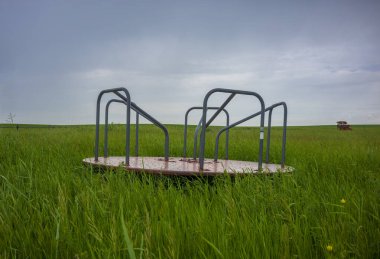 A merry-go-round, or roundabout, sits dormant in a vast grassland in North Dakota during an overcast day. 