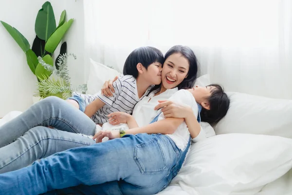 Güzel, mutlu, Asyalı bir aile sıcak bir evde. Oğlan ve kız, anneyi zevkle öperler, rahatlar ve yatak odasında birlikte oynarlar. Mutluluk ilişkisi ve ebeveynler ve çocuklar arasında sevgi bağı.