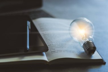 Parlak ampul, kitap, tablet ve kopya alanı olan laptop. Kendi kendine öğrenme ya da eğitim bilgisi ve iş eğitimi kavramı. İnternette öğrenme veya evde e-öğrenme fikri.