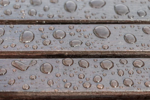 Su damlalarıyla kaplı ahşap tahtalar, yağmurlu hava için arka plan. Islak kahverengi tahtalar kapanır. Seçici odak