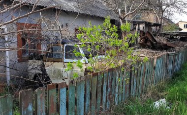Şehrin terk edilmiş eski bir evinin yakınındaki ahşap bir çitin arkasında parçalanmış eski bir araba.