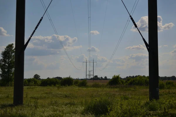牧草地の青い夏の空に対する高電圧の電柱と送電線 — ストック写真