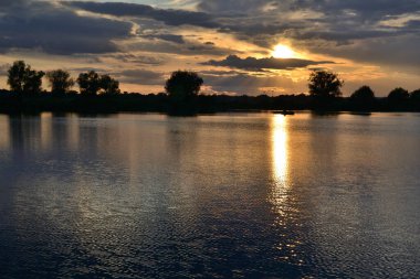 Yaz günbatımında gölde ağaçların siluetleriyle