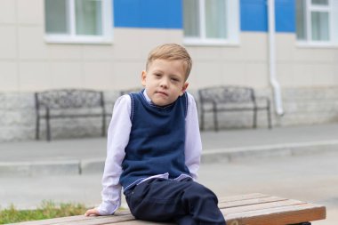 Okulun yakınındaki bir bankta güneşli bir sonbahar gününde okul üniformalı tatlı bir birinci sınıf öğrencisi oturuyor. Kutlama 1 Eylül 'de. Bilgi toplama günü. Seçici odak