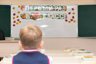 Birinci sınıftaki çocuk, okuldaki bilgi gününde sınıftaki masasında oturuyor. Tahtada bir yazı var, birinci sınıfta ilk kez bir yazı. Seçici odaklanma. Yakın plan.