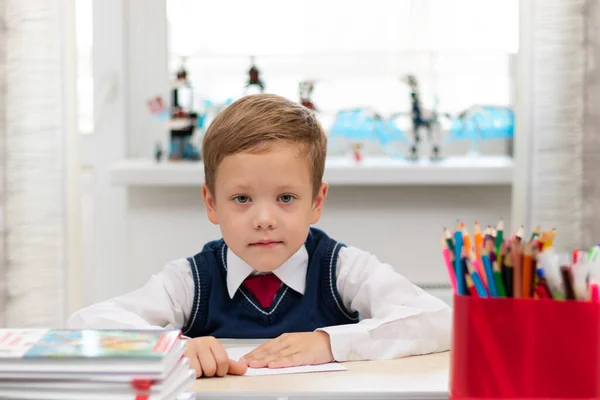一个在家里穿着校服的一年级可爱男孩在课间休息时独自坐在办公桌前 制造了一架纸飞机 有选择的重点 肖像画 — 图库照片