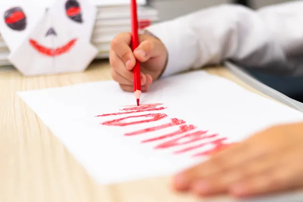 一年级男孩坐在白桌旁 用一支红色明亮的铅笔在白纸上画了一张明信片来庆祝光晕假期 有选择的重点 Bokeh — 图库照片