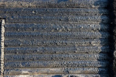 Güneşli bir yaz gününde, kırsal bir ağaç evin siyah, yanmış duvarı. Kömür. Dokulu yüzey. Yakın plan.